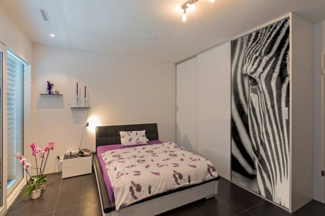 In der Mitte ein Designerbett und rechts ein Einbauschrank mit einer besonderen Zebra-Schiebetüre