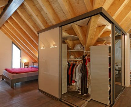 Schrank unter der Dachschräge. welcher sogar um ein Eck herum geht. Der Schrank besteht aus einer Schiebetürfront über Eck aus verspiegelten SChiebetüren und weißen Hochglanzschiebetüren. Auf diesem Bild ist der geöffnete Schrank unter der Dachschräge abgebildet, der einen Ausblick auf dessen Innenleben aus Schieberegalen und unserem Säulensystem kombiniert mit Kleiderstangen und in einer doppelten Tiefe unter der Dachschräge abgebildet.